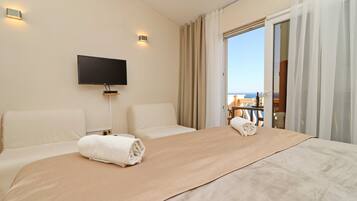 Une chambre d’hôtel avec un grand lit, un téléviseur à écran plat fixé au mur et un balcon offrant une vue sur la mer.