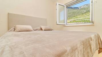 Un dormitorio con cama, dos almohadas y ventana con vista a un paisaje verde.