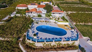 Vue aérienne d'un complexe hôtelier doté d'une grande piscine, de plusieurs villas pour les clients et de rangées de vignes.