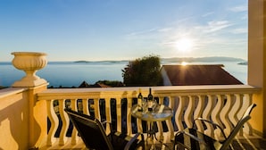 A balcony with a view of the sea, a table with glasses and a bottle, and a decorative urn.