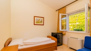 A bedroom with a bed, a desk, a dresser, a radiator, and a window with a view of greenery.