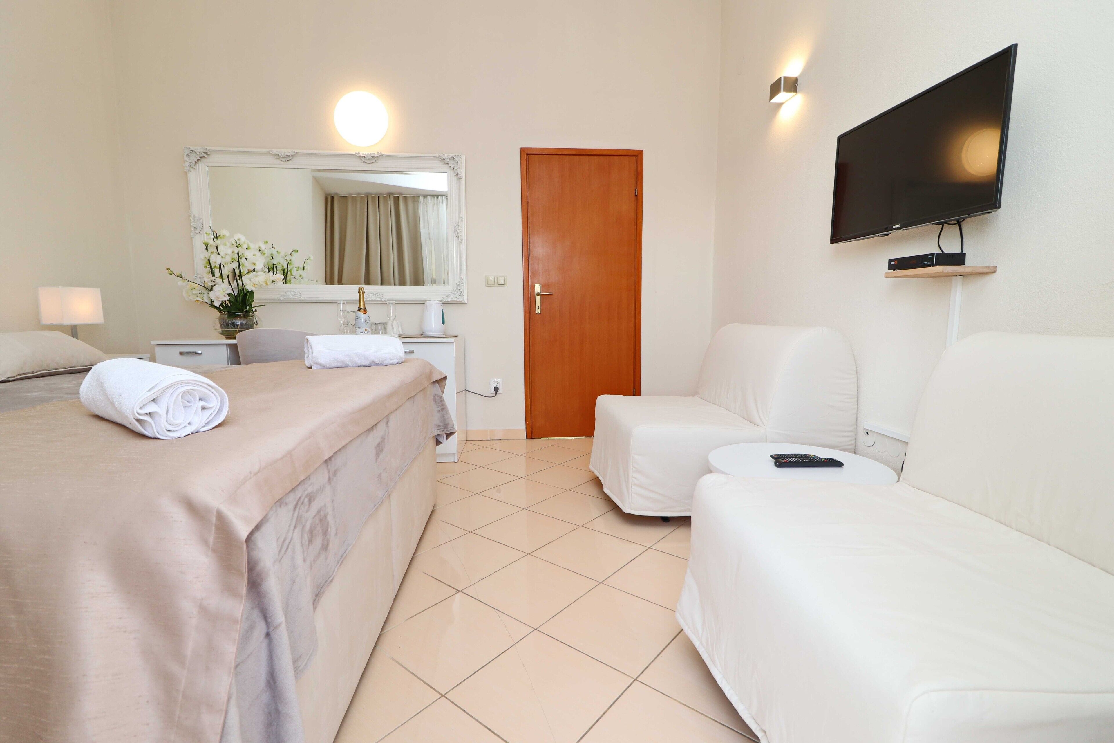 A hotel room with a bed, a sofa, a TV, and a mirror.