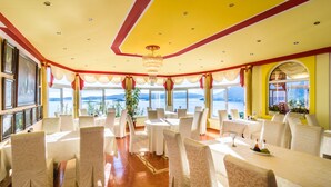 Une salle de banquet avec des tables rondes, des chaises blanches et un grand lustre.