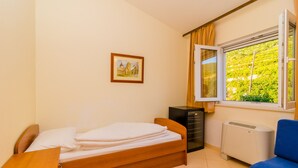 Une chambre à coucher comprenant un lit, un bureau, une commode, un radiateur et une fenêtre donnant sur un paysage verdoyant.