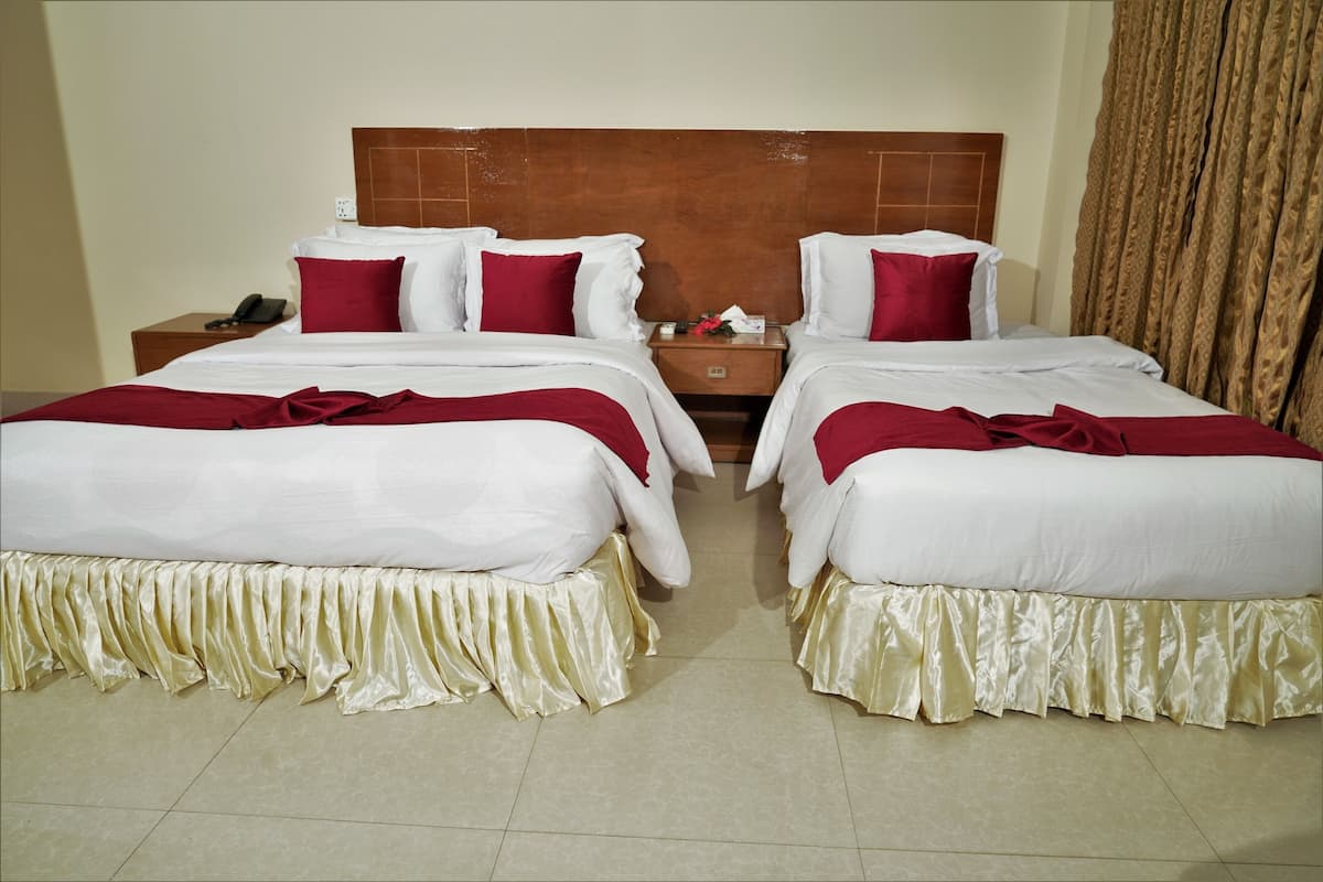 A hotel room with two beds, each with white linens and red pillows, a wooden headboard, and a small bedside table with a phone and a tissue box.