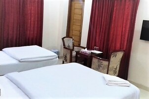 Una habitación de hotel con dos camas, una silla de madera, una mesita pequeña y cortinas rojas.