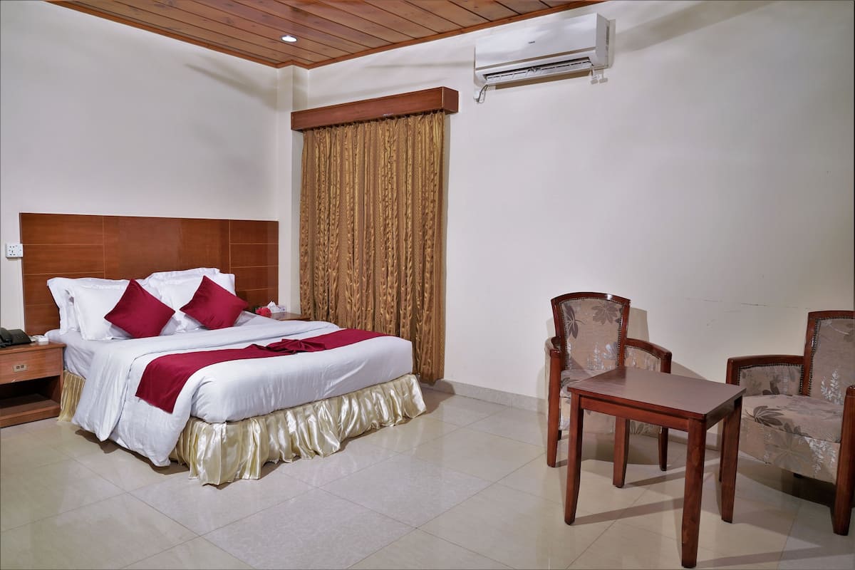 A hotel room with a bed, a wooden headboard, a table, and two chairs.