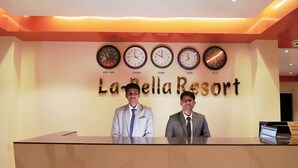 A reception desk at La Bella Resort with clocks displaying times from New York, London, Dhaka, Dubai, and Delhi. - La Bella Resort (Cox's Bazar)