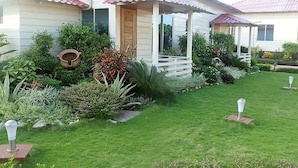A house with a porch, surrounded by a well-maintained garden with various plants and a lawn. - La Bella Resort (Cox's Bazar)