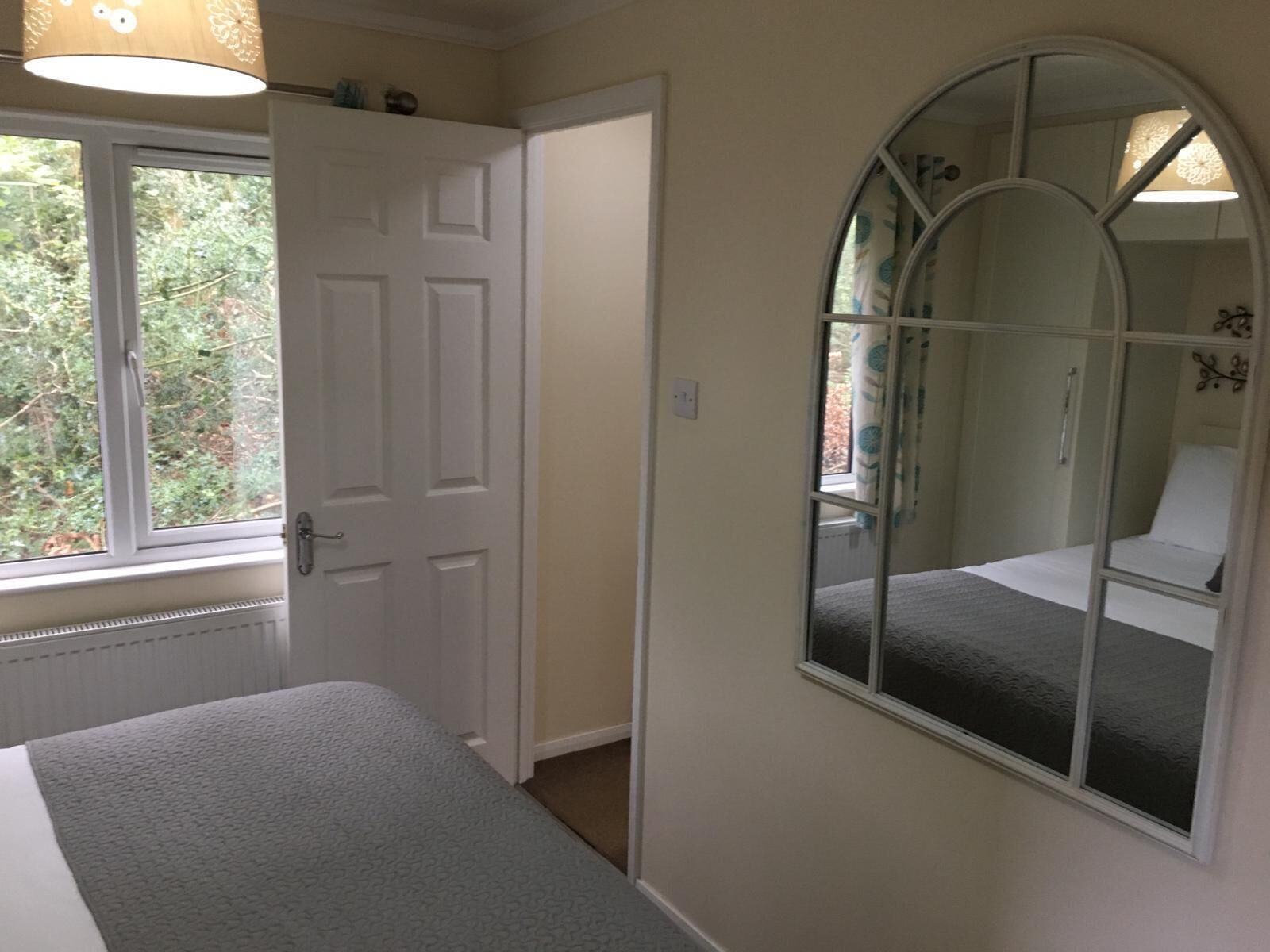 A bedroom with a bed, a window, a door, and a mirror.