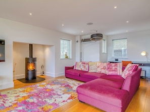 A modern living room with a wood-burning stove, a pink sofa, and a colorful rug. - 5 bedroom accommodation in Somerford Keynes, near Cirencester (Somerford Keynes, near Cirencester)