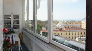 A room with a large window overlooking a cityscape, a white cabinet with glass doors, and a small table with a vase of flowers.