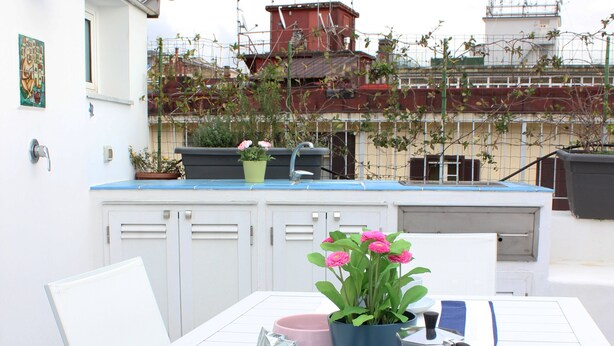 A dining table set with a blue and white striped tablecloth, a white cup, a pink pot with flowers, and a silver kettle.