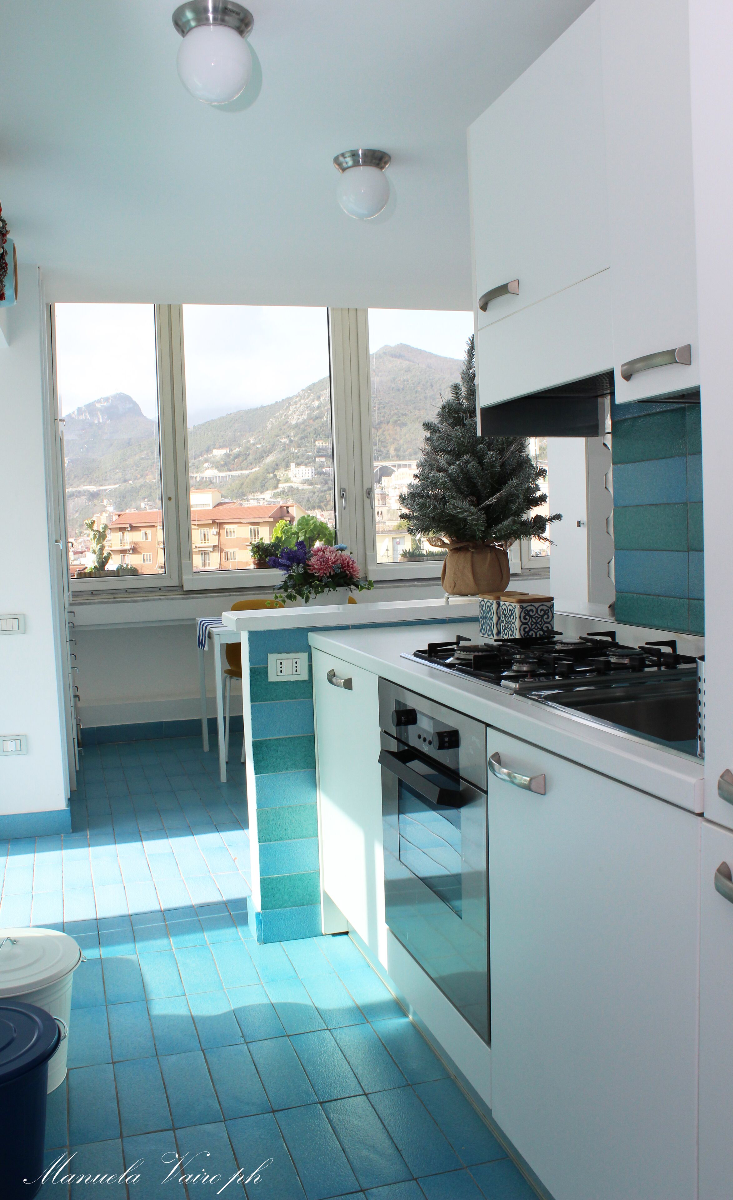 Eine moderne Küche mit großem Fenster, einem Blumentopf und Blick auf eine Brücke und Berge.