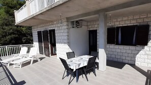 An outdoor patio with a table and chairs, a covered seating area, and a balcony with white railings. - Apartment Classic Korčula - Two Bedroom Apartment with Terrace and Sea View (Korcula)