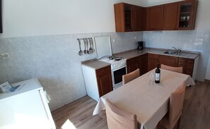 Cocina compacta con estufa, lavamanos y armarios de madera. Se sirve una mesa con una botella y un vaso.