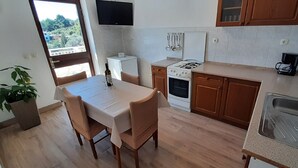 A compact kitchen with a dining area, a TV mounted above the stove, and a view of greenery outside. - Apartment Classic Korčula - Two Bedroom Apartment with Terrace and Sea View (Korcula)