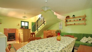 Un comedor con una mesa y sillas de madera, un sofá verde, una escalera y una cocina con armarios de madera.
