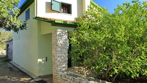 Una casa de dos pisos con entrada de pared de piedra, techo verde y una ventana con persianas verdes.