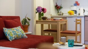 Une pièce chaleureuse avec un canapé rouge, une petite table sur laquelle se trouvent une tasse et une télécommande, et un coin cuisine avec une table à manger et des chaises.