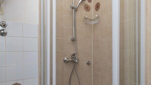 Un espace douche doté d’une porte en verre, d’un pommeau de douche à main et d’un robinet mural.