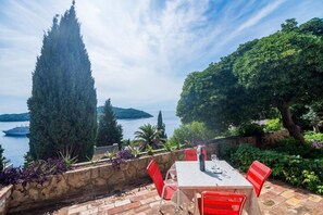 A patio with a table and chairs overlooking a body of water, with a boat visible in the distance. - Apartment Charming Arena - One Bedroom Apartment with Terrace and Sea View (Dubrovnik)