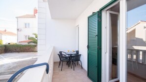 A balcony with a table and chairs, a sliding glass door, and a view of neighboring buildings. - Apartment Budimir - Two Bedroom Apartment with Balcony (Podstrana)