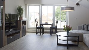 Ein modernes Wohnzimmer mit einer Couch, einem Esstisch mit Stühlen, einem Fernseher und einer Zimmerpflanze.