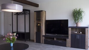 Ein modernes Wohnzimmer mit Flachbildfernseher, Holzregalen, einem schwarzen Couchtisch und einer Topfpflanze.