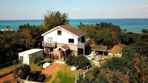 Una casa de dues plantes amb un balcó, envoltada d'arbres i vista a l'oceà.