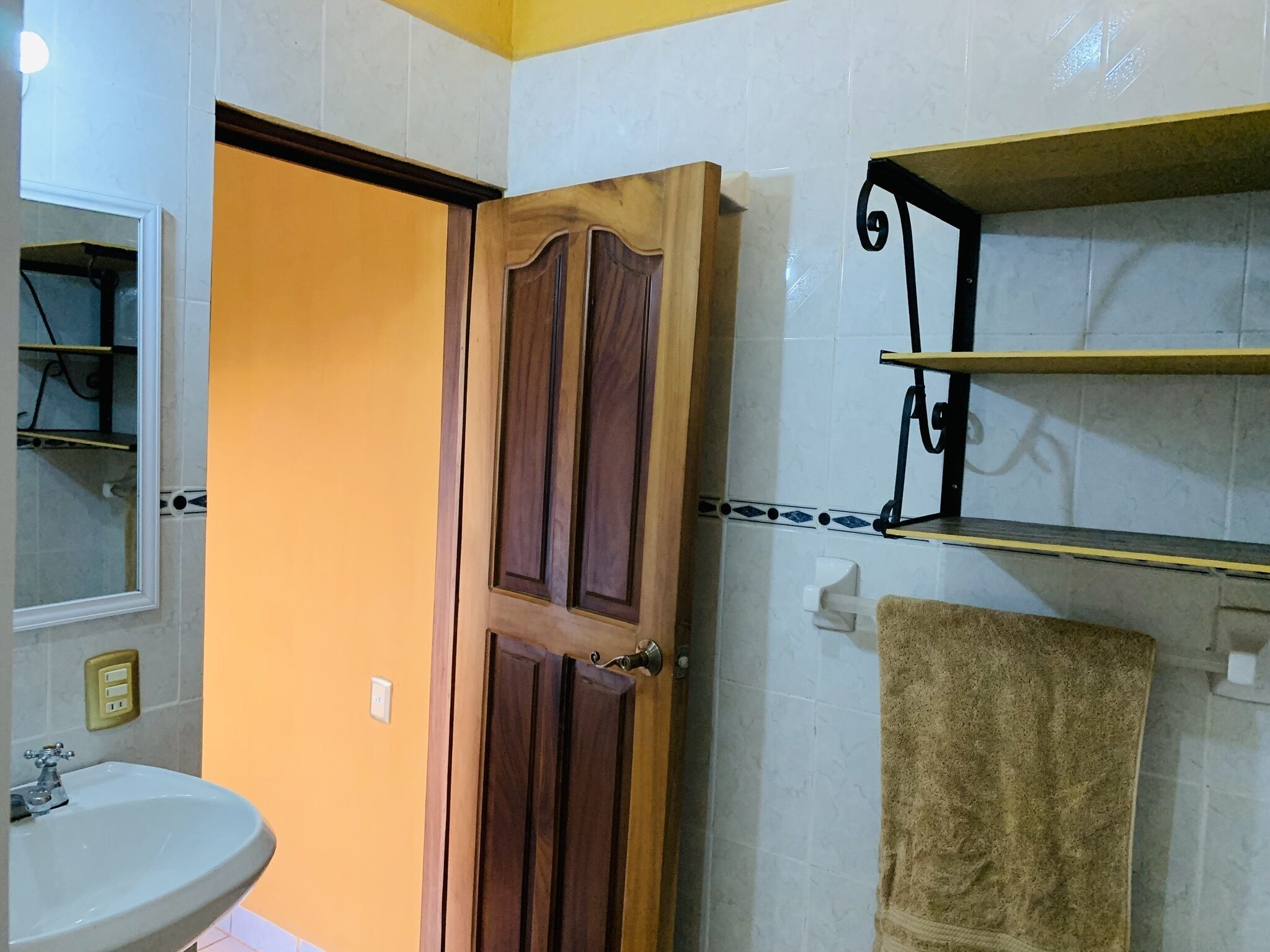 A bathroom with a wooden door, a sink, a towel, and a shelf with a towel.
