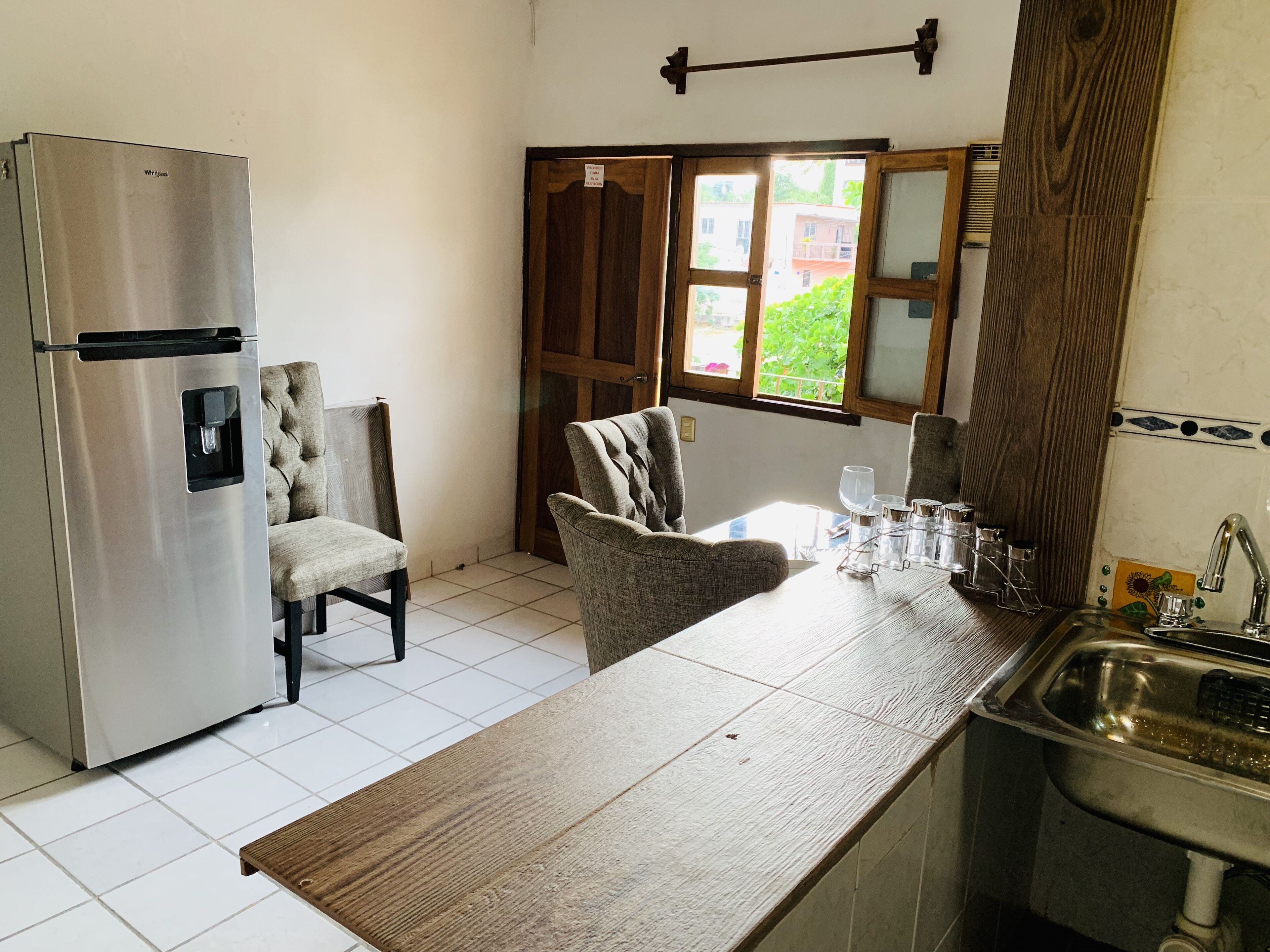 Una cocina compacta con un refrigerador de acero inoxidable, una mesa de comedor de madera y un lavamanos.