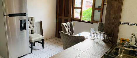 Una cocina compacta con un refrigerador de acero inoxidable, una mesa de comedor de madera y un lavamanos.
