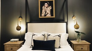 A bedroom with a large bed, two bedside tables, a framed portrait on the wall, and two wall-mounted lamps. - Luxury Cottage in Historic Beauregard Town  (Baton Rouge)