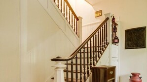 Una escalera de madera con barandilla blanca, un mueble de madera pequeño y un contenedor rojo en el suelo.