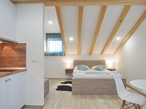 A bedroom with a wooden ceiling, a bed with two pillows, a bedside table with a lamp, and a white chair. - Apartments Sweet Escape - Studio Apartment with Terrace and Sea View (2) (Dubrovnik)