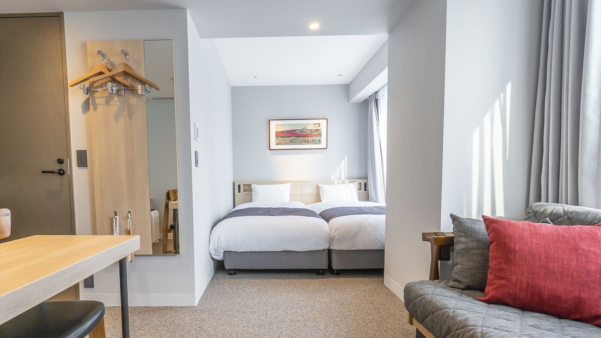 A bedroom with a bed, a desk, a chair, a sofa, and a painting on the wall.