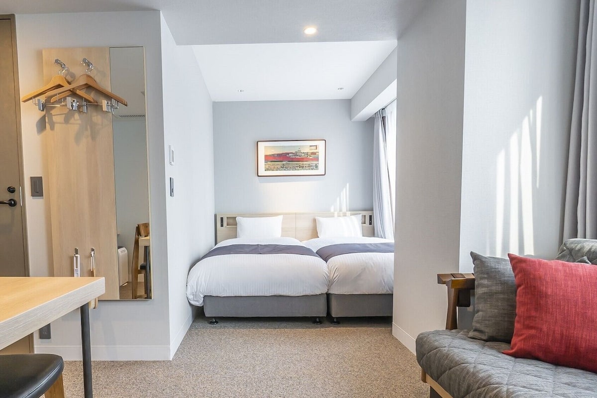 A bedroom with a bed, a desk, a chair, a sofa, and a painting on the wall.