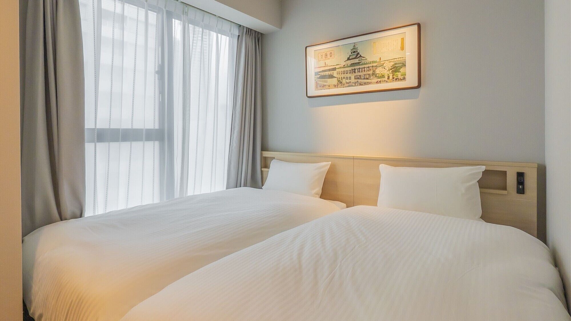 A hotel room with two beds, a large window with sheer curtains, a framed picture on the wall, and a wooden headboard.