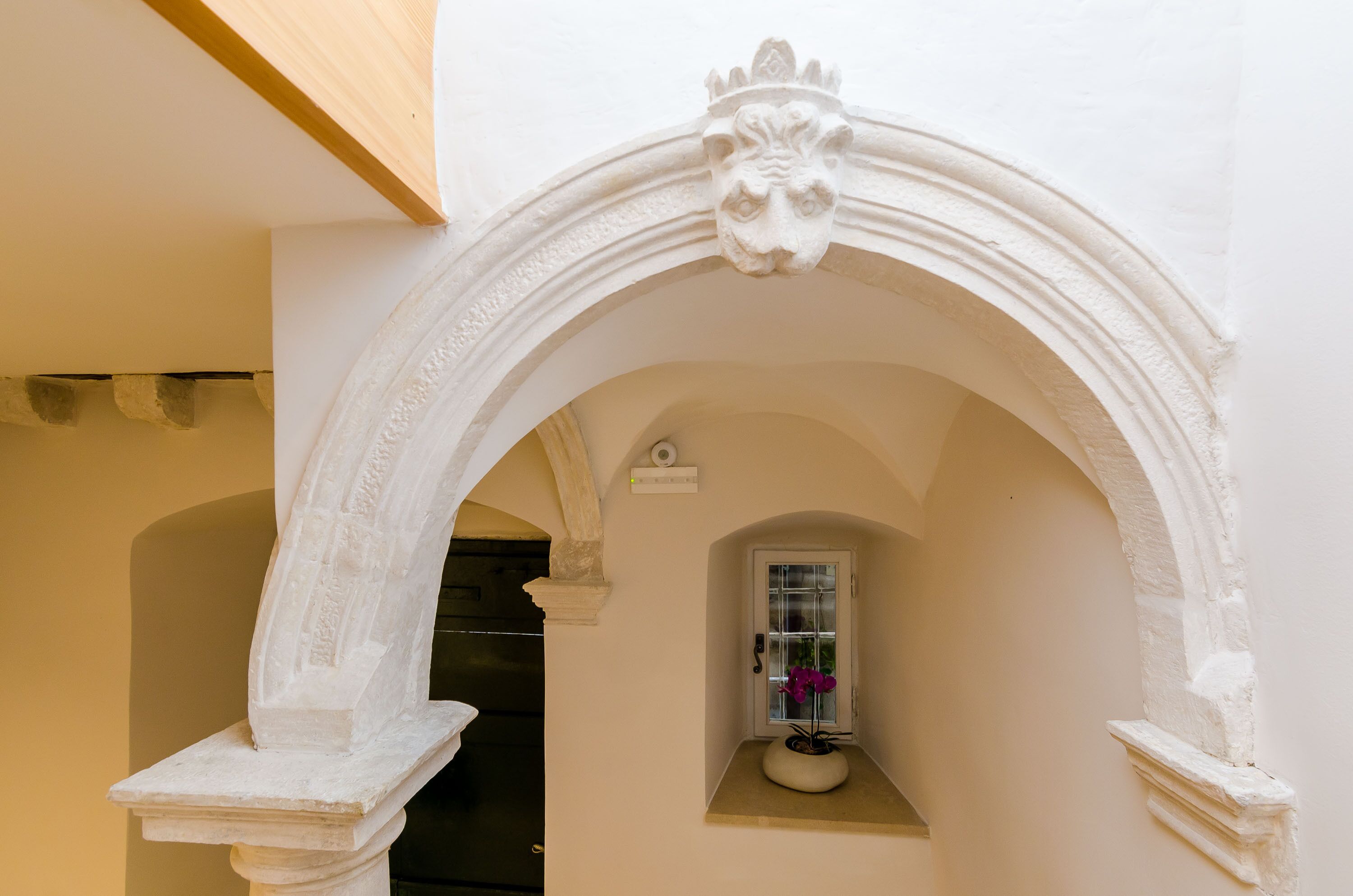 An arched doorway with a decorative stone frame and a small window with a potted plant.