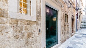 A stone building with a dark door, a window with bars, and a narrow street.