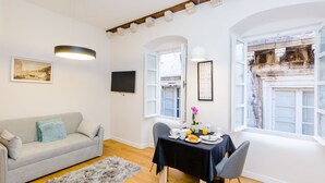 A modern living room with a sofa, a dining table set with plates, cups, and a vase of flowers.