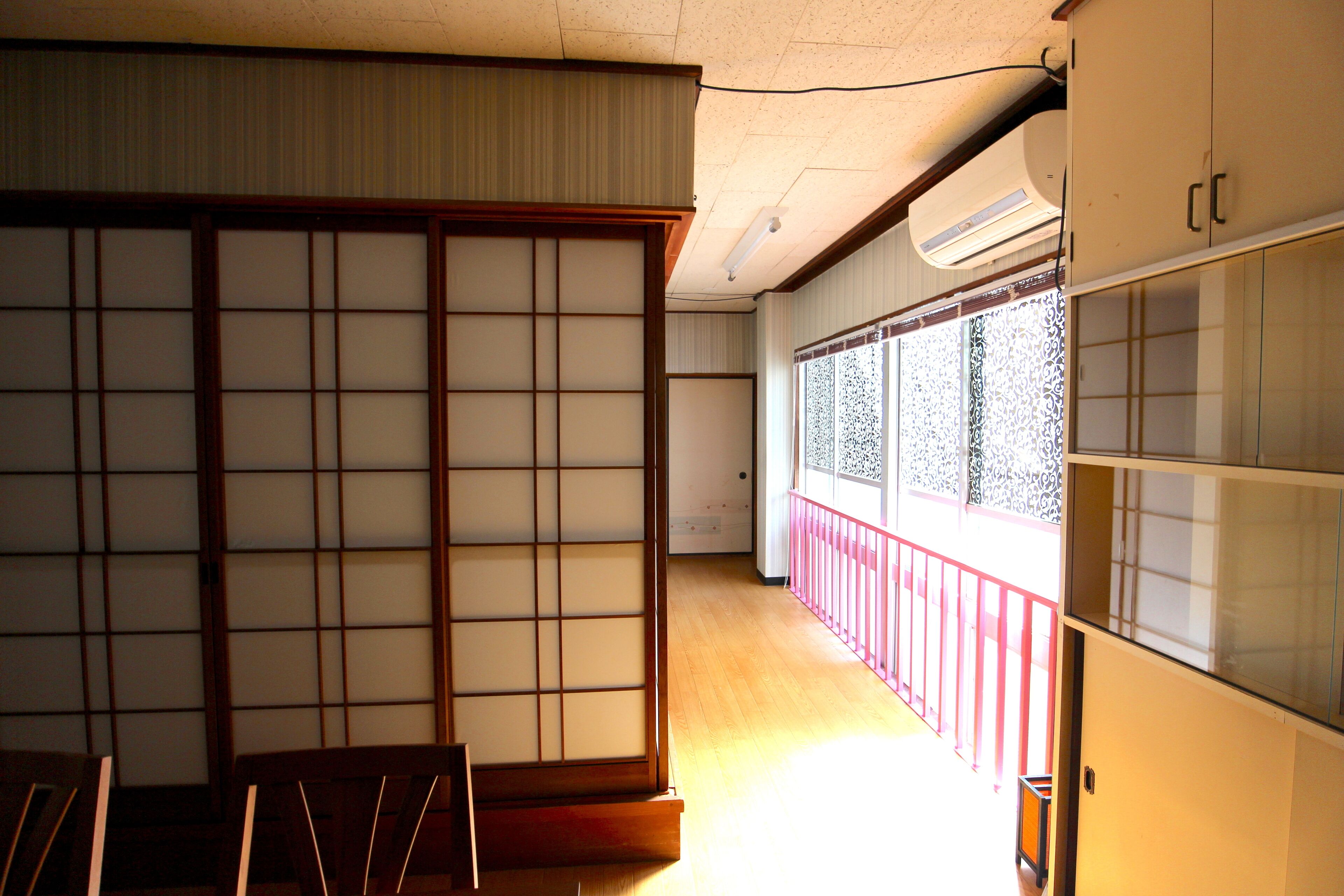 Une pièce de style japonais traditionnel, avec des portes coulissantes, un plancher en bois et une vue sur une rambarde rouge à l’extérieur.