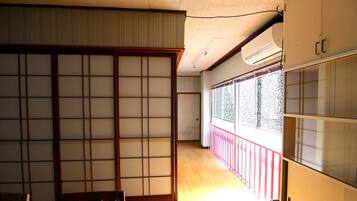 Une pièce de style japonais traditionnel, avec des portes coulissantes, un plancher en bois et une vue sur une rambarde rouge à l’extérieur.