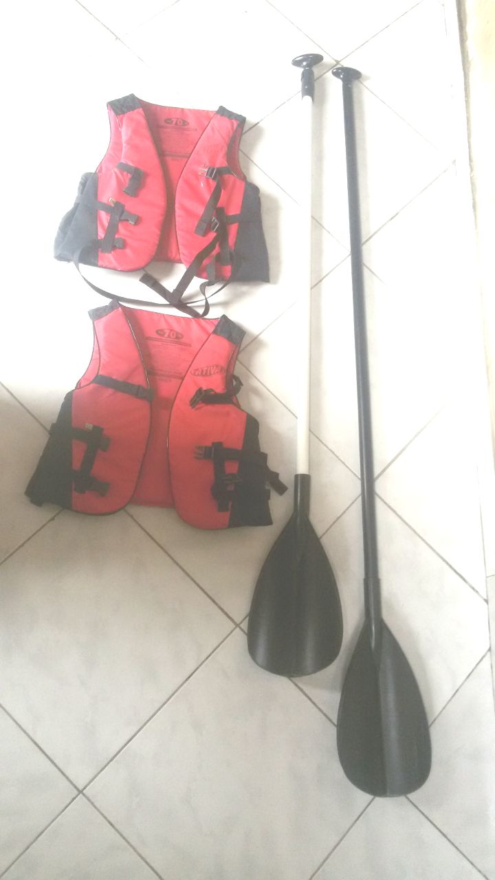 A tiled floor with four red life jackets hanging on the wall and two black paddles leaning against the wall.