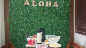 Una mesa con comida y una botella, frente a un muro verde con la palabra 'ALOHA' escrita.