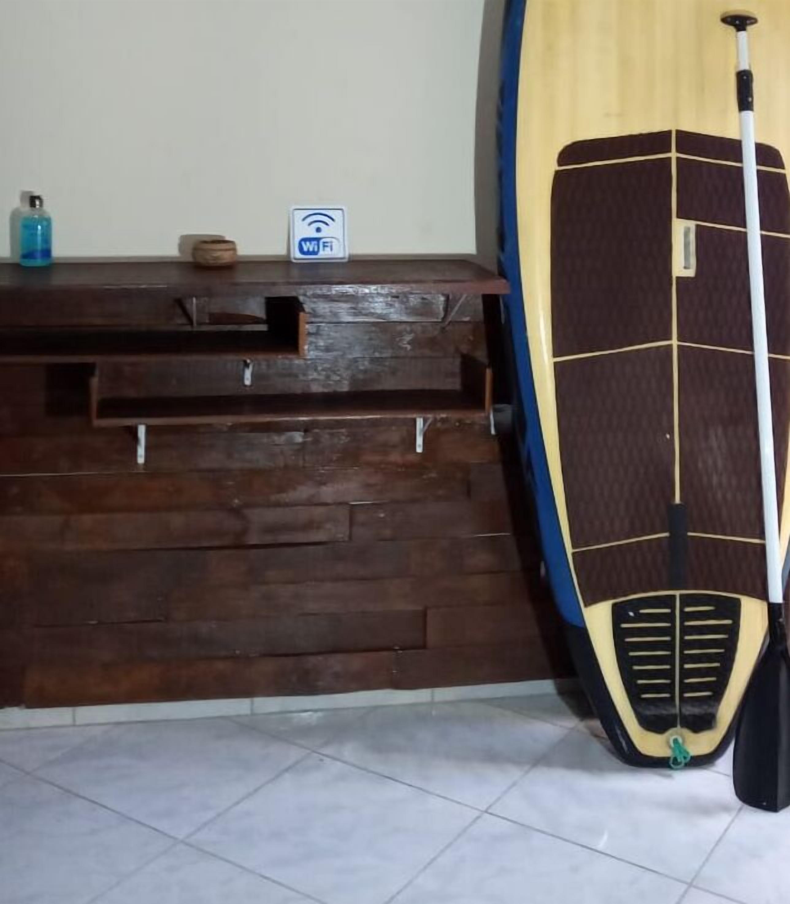 Een houten receptiebalie met een Wi-Fi sign, een fles handzeep en een paddleboard dat tegen de muur staat.
