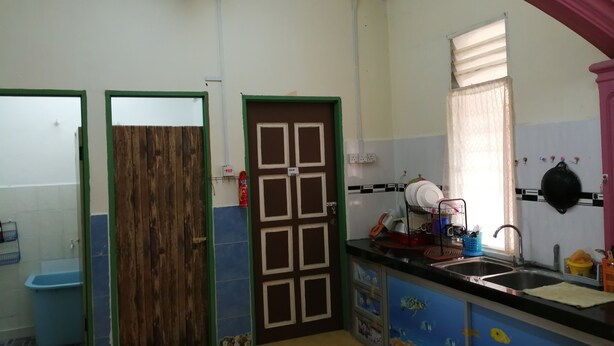A kitchen with a sink, a window with a curtain, and a door with a wooden panel. - Guest house transit to Langawi Island (Kuala perlis)
