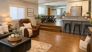 A modern living room with a leather sofa, a dining area with a wooden table, and a kitchen with a marble countertop.