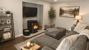 A cozy living room with a fireplace, a flat-screen TV, a couch, and a painting of a lake. - Walk to Town & Lake · Spacious Family Home (McCall)
